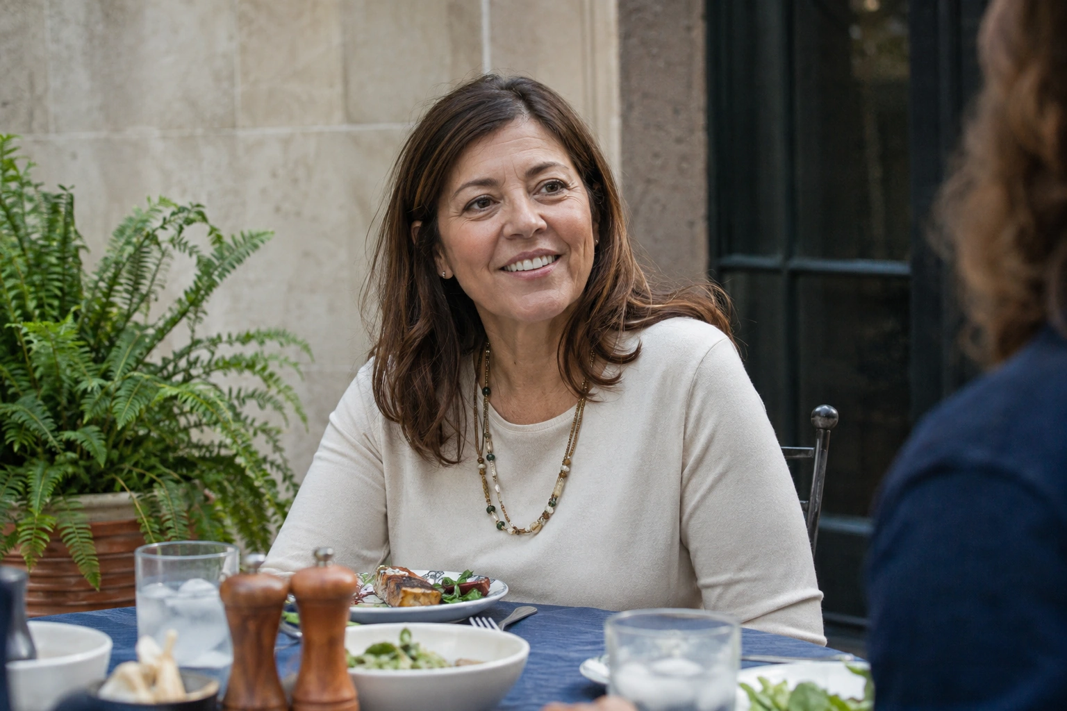 A middle-aged woman enjoying a conversation over a meal outdoors.