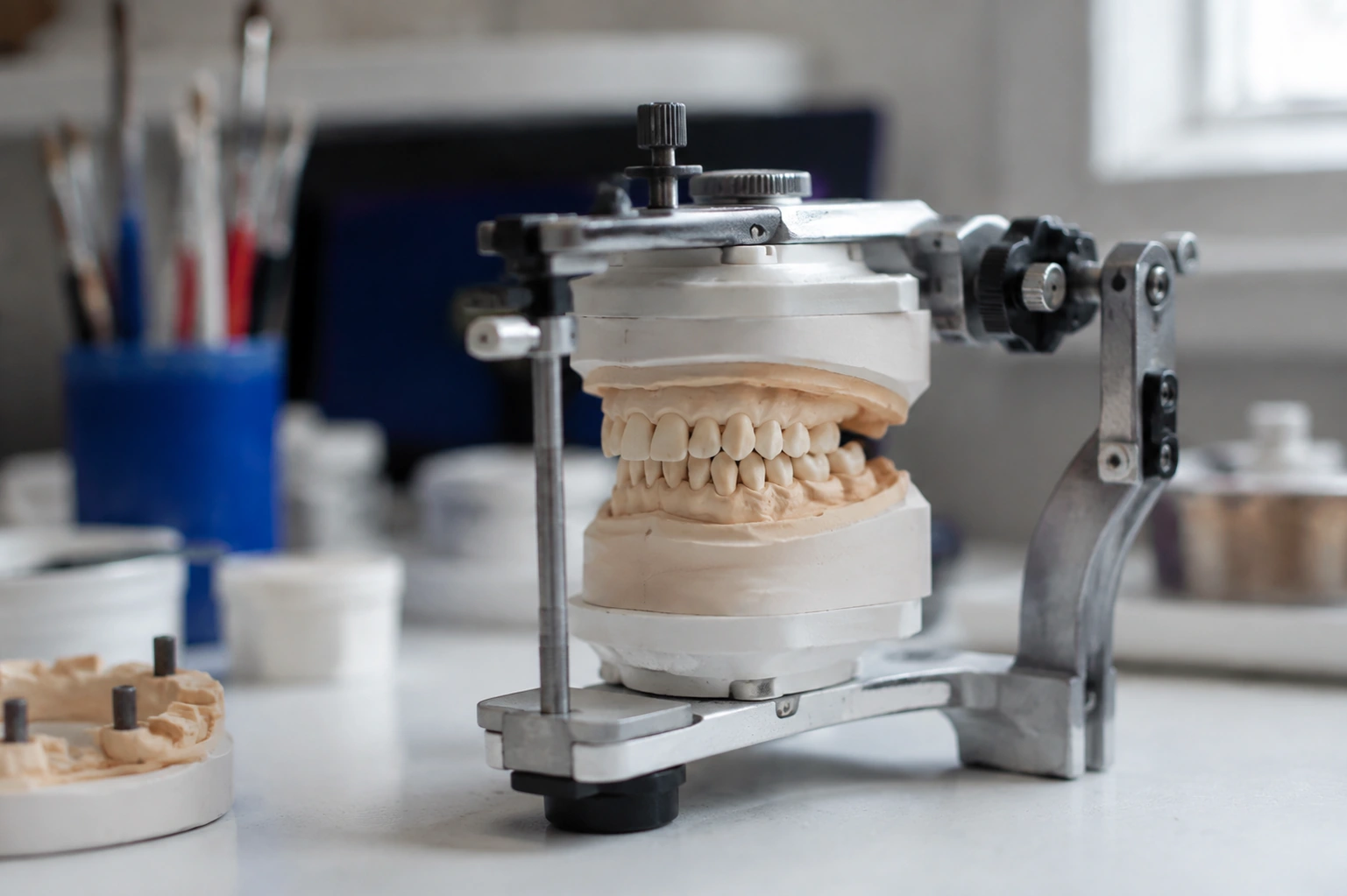 A pair of realistic articulated upper and lower dental casts on a compact bench articulator.