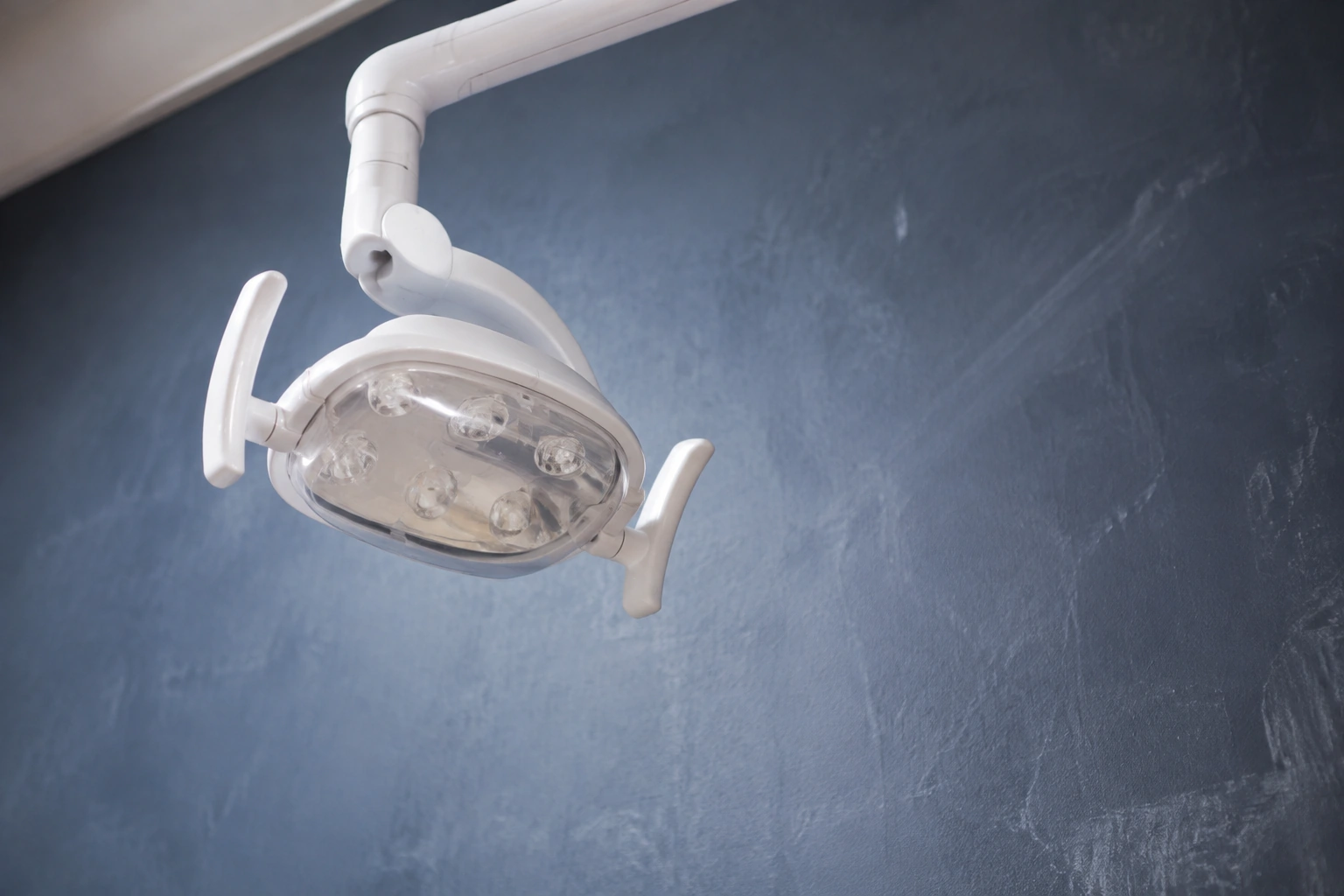 Close detail of a clean dental examination light and its handle above a chalk wall.