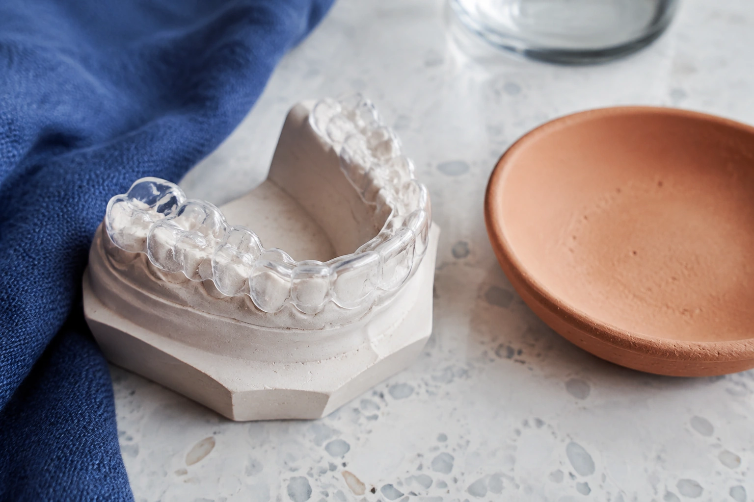 A transparent nightguard resting on a shaped dental cast beside a soft clay ceramic dish.